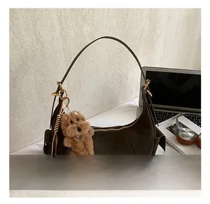 Detailed view of brown faux suede hobo bag with plush dog charm and spare shoulder strap