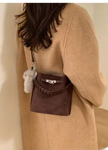 Detail of dark brown suede bucket bag featuring woven handle and plush bunny charm accessory