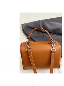 Detail of a brown leather cylindrical box bag with silver hardware and adjustable strap