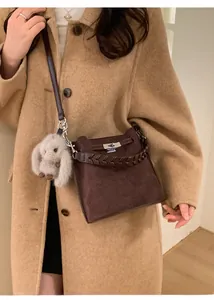 Detail of dark brown suede bucket bag with woven handle and plush rabbit pendant