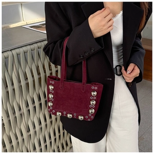 Détail du sac à bandoulière bordeaux en daim avec rivets argentés porté par un mannequin