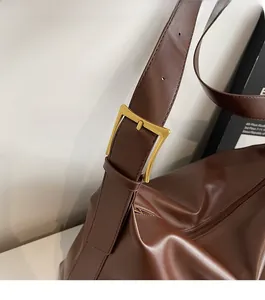 Detail of a brown leather shoulder bag featuring a square gold alloy buckle on the strap
