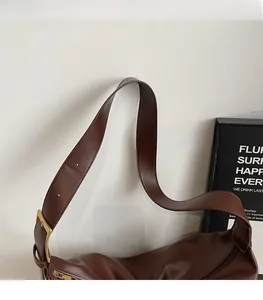 Detail of dark brown leather shoulder bag featuring adjustable wide strap and gold hardware