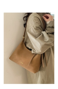 Close-up of brown textured leather hobo bag with gold logo on khaki coat shoulder