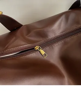 Detailed close-up of dark brown leather tote bag with smooth golden metal zipper slider