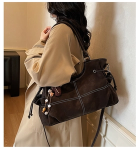 Close-up of brown faux leather tote bag with white contrast stitching and tassel charm