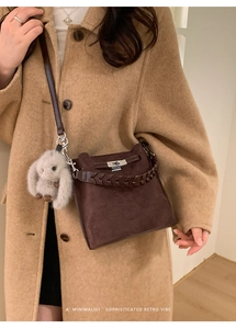 Detail of retro leather bucket bag with woven handle and plush rabbit charm on coat