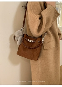 Detail of a brown suede bucket bag with silver clasp, rabbit charm and woven handle