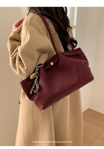 Side view of a burgundy leather tote bag with a leopard print pom-pom charm on a model