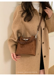 Brown suede bucket bag detail showing woven handle and metallic twist lock on coat