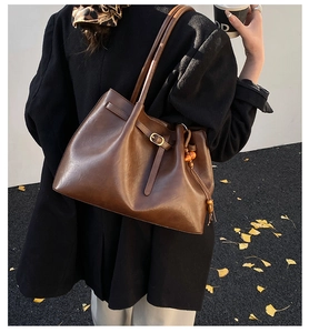 Détail du sac cabas vintage en cuir marron avec plis et pompon décoratif en perles de bois