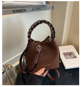 Close-up of a dark brown bucket bag with woven handle and gold brand hardware detail