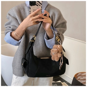 Detailed view of a black suede dumpling bag with a cute brown plush puppy charm