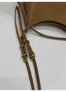 Detail of adjustable shoulder strap with golden metal buckles on brown leather bag
