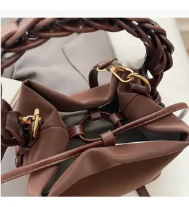 Detail of brown matte leather bucket bag with woven handle and gold metal ring hardware