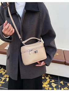 Detail of a beige minimalist box bag with silver twist lock and dual zipper design