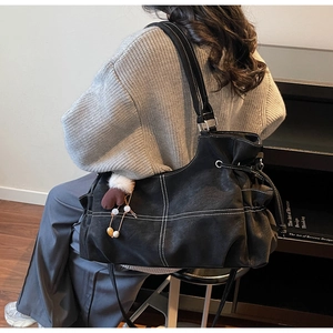 Detail of black leather tote bag with white contrast stitching and brown glove pendant
