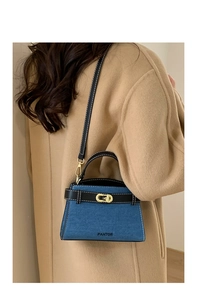 Close-up of denim blue and black leather trapezoid handbag with gold metal lock detail