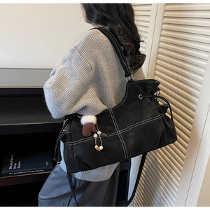 Detail of black suede tote bag with white contrast stitching and plush glove charm