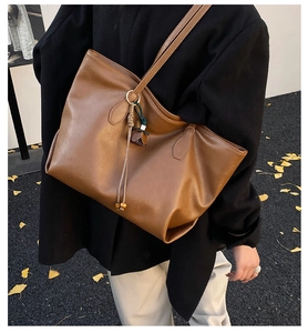 Detailed view of retro brown faux leather tote bag with tassel charm worn outdoors