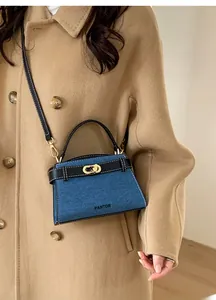 Detail view of navy denim handbag with black leather handles and gold-tone twist lock buckle