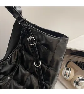 Detail of glossy quilted leather texture and silver buckle on a black tote bag