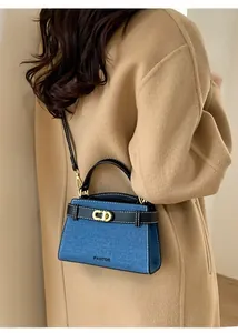 Detail of blue denim handbag with leather trim and gold twist lock worn with a beige coat