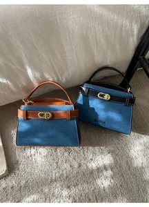 Detail of blue denim and leather handbags with gold oval twist lock in soft sunlight