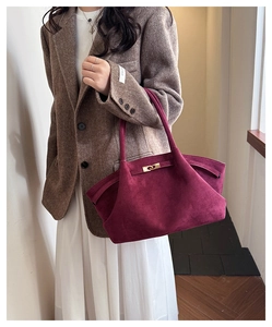 Detail of burgundy suede tote bag with gold buckle closure shown on model shoulder