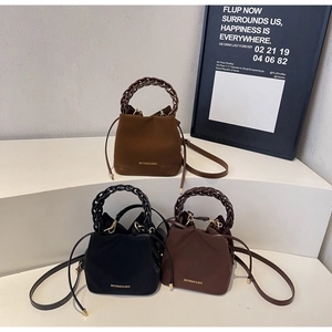 Three minimalist bucket bags with woven handles in light brown, black, and dark coffee tones