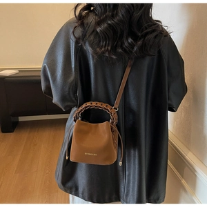 Detail view of brown leather bucket bag with braided handle and adjustable crossbody strap