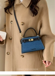 Detail of a denim blue mini handbag with black leather straps and golden clasp hardware