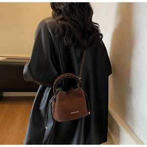 Close-up of brown leather bucket bag with braided chain handle and gold foil branding