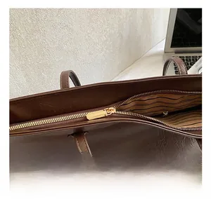 Detail view of smooth golden zipper on dark brown leather tote bag with striped lining