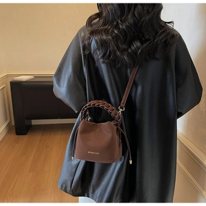Detailed view of brown bucket bag with thick braided handle and gold brand lettering