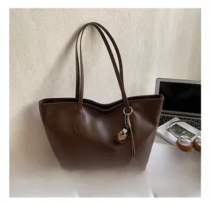 Deep brown leather tote bag detail with tassel charm and office lifestyle props