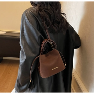 Close-up of brown suede bucket bag featuring woven leather handle and drawstring closure