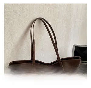 Close-up of a large dark brown leather tote bag with long handles and decorative tassel