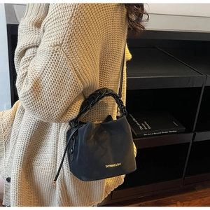 Detail of black bucket bag with gold lettering and woven chain handle worn by a model