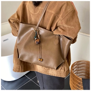 Close-up of brown PU leather tote bag featuring tassel charm and lychee texture detail