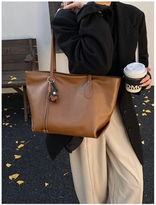 Close-up of brown PU leather tote bag with wooden bead tassel in autumn street setting