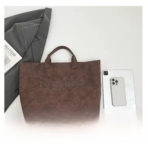 Detail of dark brown tote bag with studded lettering beside an iPad for size reference