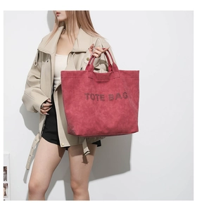 Detailed view of deep red suede tote bag with TOTE BAG lettering held by a model