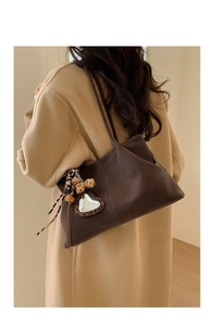 Brown suede tote bag detail featuring leopard heart charm and ribbon on model shoulder