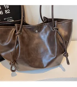 Detail of dark brown tote bag showing magnetic clasp closure and knotted side accents