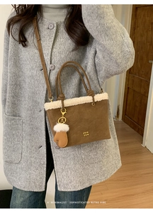 Detail of a brown suede bucket bag with white faux fur trim and mini glove charm on a coat