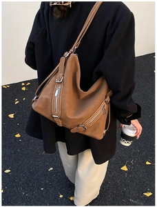 Detailed view of brown leather tote bag featuring silver zippers and metallic buckles