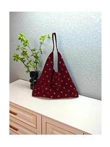 Detail of burgundy suede tote bag featuring metallic gold eyelets and shoulder strap