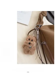 Detail of plush dog charm with pearl collar and metal tag on brown leather tote bag