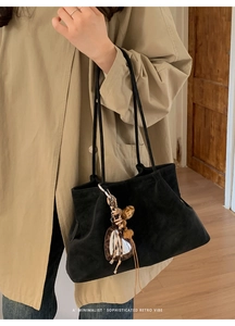 Detail of a black suede tote bag with leopard heart charm and minimalist retro design